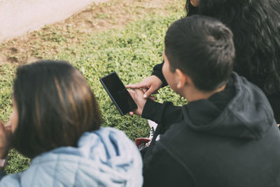 View from the back group of laughing latinos sitting on the ground in a park with a smartphone