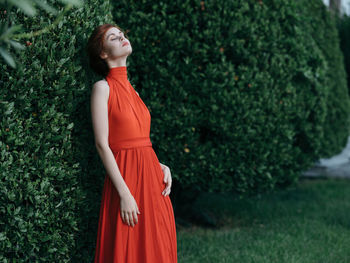 Young woman looking away while standing against plants