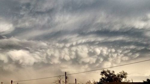 Low angle view of power lines against cloudy sky