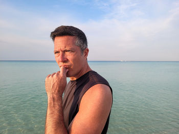 Portrait of young man looking at sea against sky