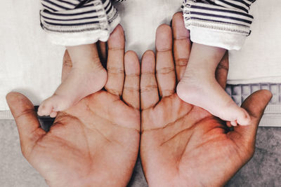 Cropped hands of parent holding baby feet on bed