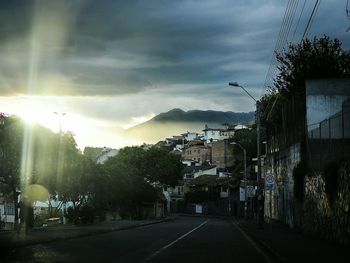 Road amidst trees against dramatic sky