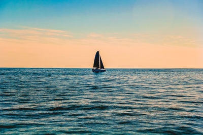 Sailboat sailing on sea against sky during sunset