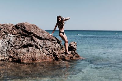 Sensuous woman standing on rock against sea at beach