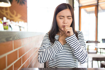 Young woman coughing while sitting in restaurant