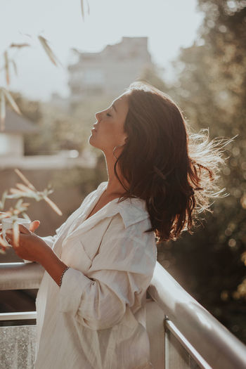 Side view of young woman holding cup in balcony
