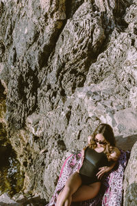 Young woman wearing sunglasses while lying on rock formation