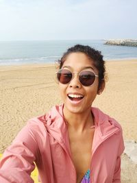 Portrait of smiling young woman standing at beach against sky