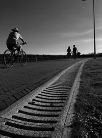 People riding bicycle on footpath against sky