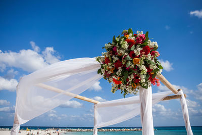 Low angle view of bouquet hanging on entertainment tent at beach against blue sky