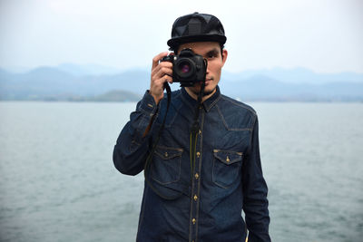Portrait of man photographing with camera against sea