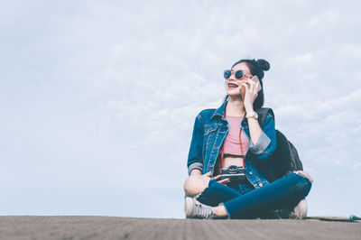 Young woman wearing sunglasses sitting on land against sky