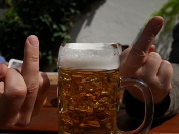 Close-up of hands showing middle fingers by beer on table
