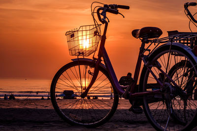 Bicycles by sea against sky during sunset