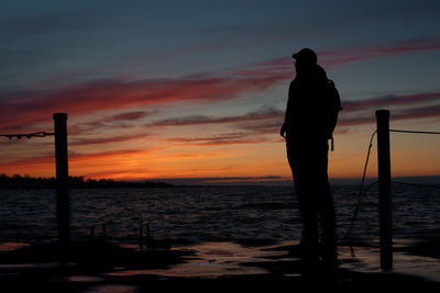 Silhouette of man standing at beach against sky during sunset