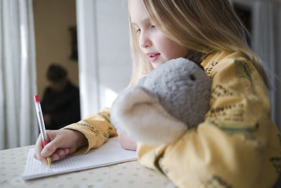 Midsection of girl writing in book at home