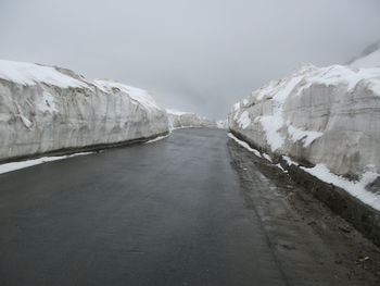 Snow covered road by mountain against sky
