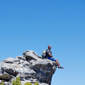 Low angle view portrait of man sitting on rock against sky