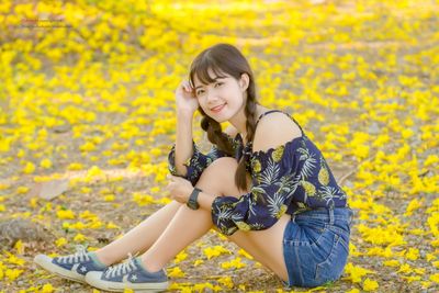 Portrait of smiling young woman sitting on yellow flowers on ground