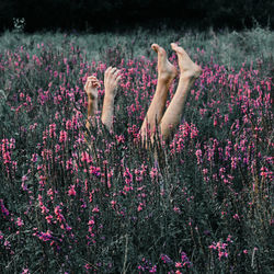 Low section of person with feet up and arms raised lying amidst plants