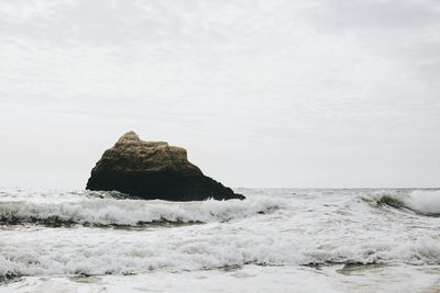 Rock formation in sea against clear sky