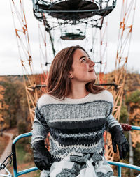 Smiling young woman looking away while sitting on ferris wheel