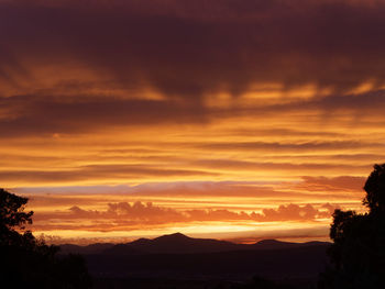 Scenic view of silhouette mountains against dramatic sky during sunset