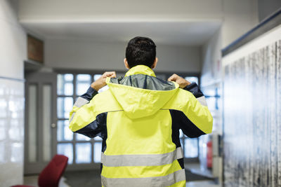 Rear view of auto mechanic student wearing reflective jacket in workshop