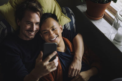 High angle view of multiracial gay couple using smart phone at home