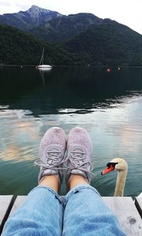 Low section of woman on pier over lake against mountains