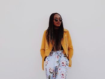 Portrait of woman wearing sunglasses while standing against white wall