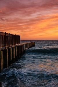 Pier over sea against orange sky