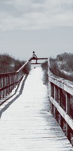 Man on footbridge in winter against sky