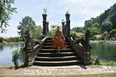 Woman walking on staircase by lake against sky