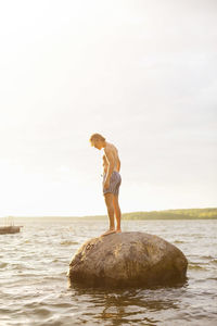 Full length side view of man standing on rock in lake against sky