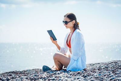 Young woman using mobile phone while sitting on beach