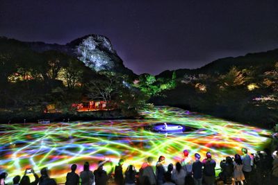Group of people watching light trails against sky at night
