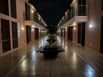 Illuminated lights on footpath amidst buildings at night