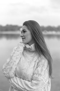 Thoughtful young woman looking away while wearing warm clothing against lake