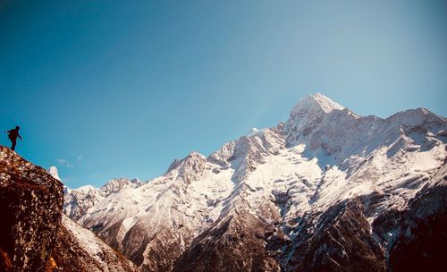 Low angle view of snowcapped mountains against clear blue sky