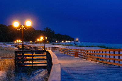 Illuminated street lights by sea against clear sky at night