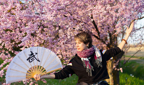 Young caucasian woman posing a wushu martial art posture in a sunny day, a pink tree in background