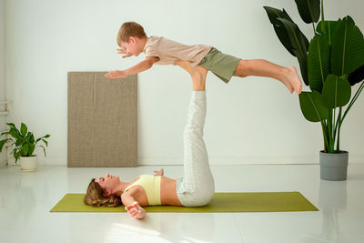 A woman, doing yoga with a child boy, lies on a sports mat