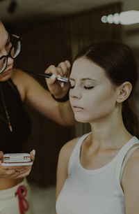 A young makeup artist applies powder with a brush to a girl s temples.