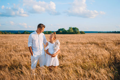 Father and daughter with dog standing on field against sky