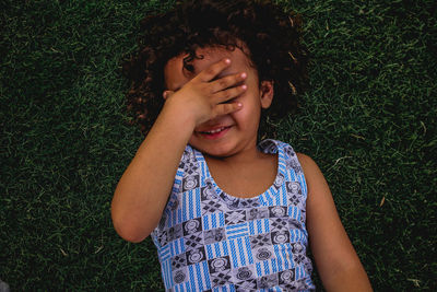 High angle view of cute girl with hands covering eyes lying on grass land