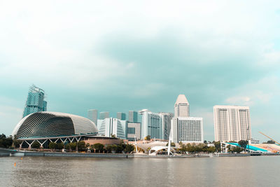 Buildings at waterfront against cloudy sky