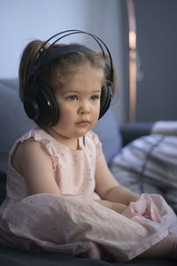 Cute girl wearing headphones sitting on bed at home