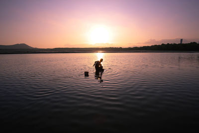 Silhouette man on shore against sky during sunset