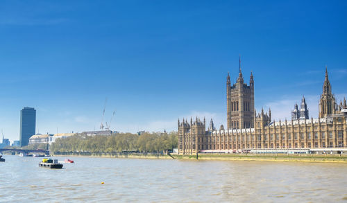 Boats in river by buildings against sky